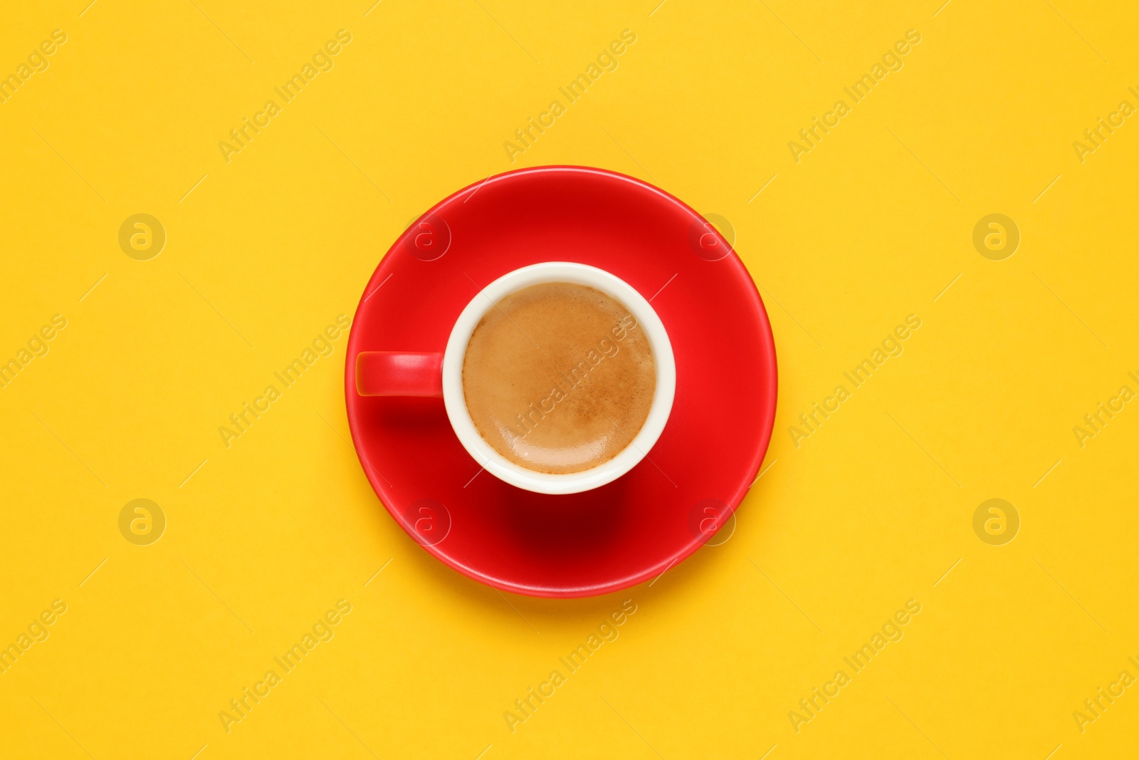 Photo of Aromatic coffee in red cup on yellow background, top view