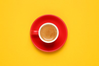 Photo of Aromatic coffee in red cup on yellow background, top view