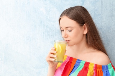 Young woman drinking lemon juice on color background