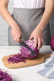 Photo of Woman cutting fresh red cabbage at white wooden table, closeup