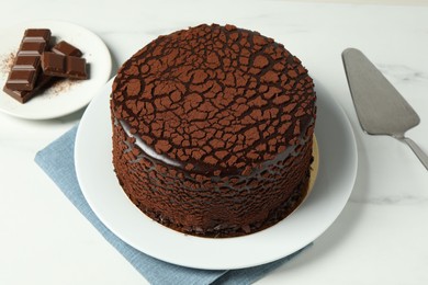Photo of Delicious truffle cake, chocolate pieces and server on white marble table