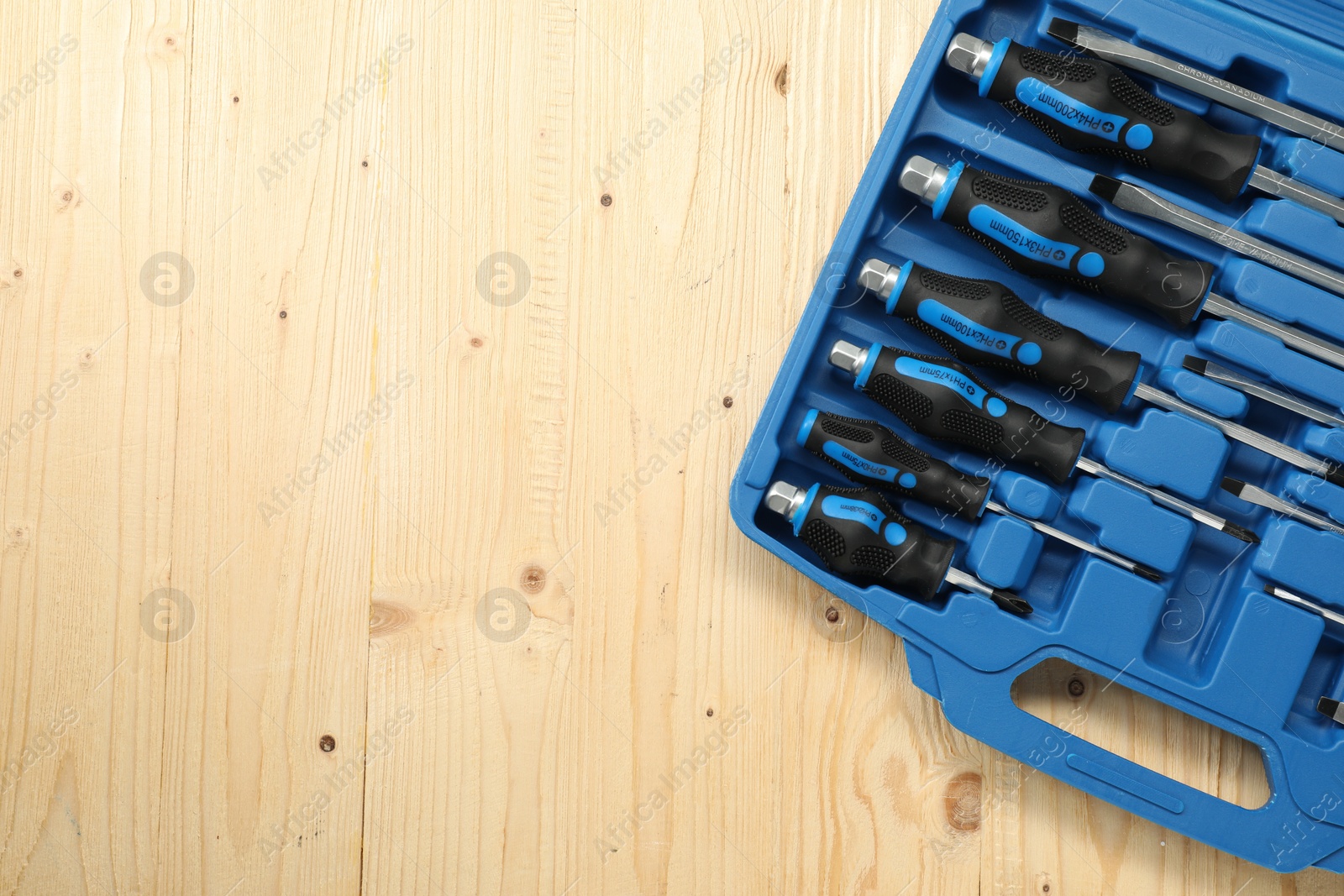 Photo of Set of screwdrivers in open toolbox on light wooden table, top view. Space for text