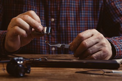 Professional jeweler working with gemstone at wooden table, closeup