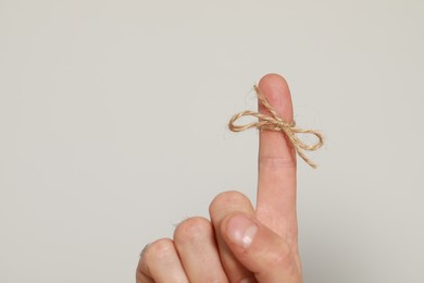 Man showing index finger with tied bow as reminder on light grey background, closeup