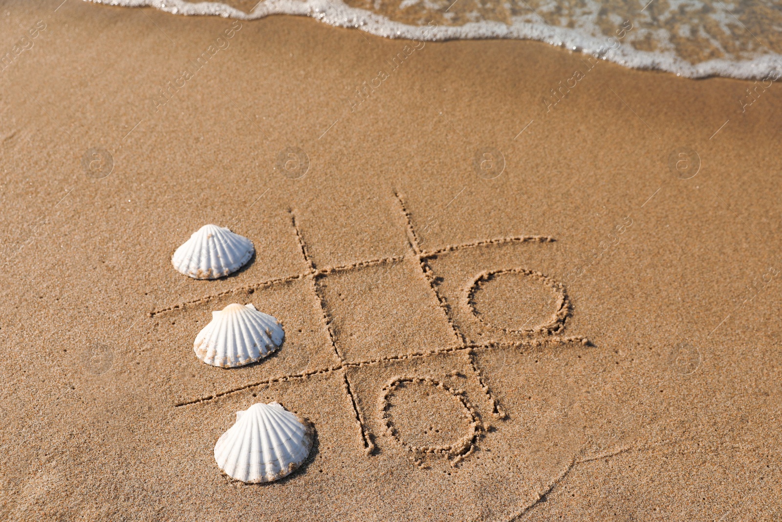 Photo of Playing Tic tac toe game with shells on sand near sea, above view