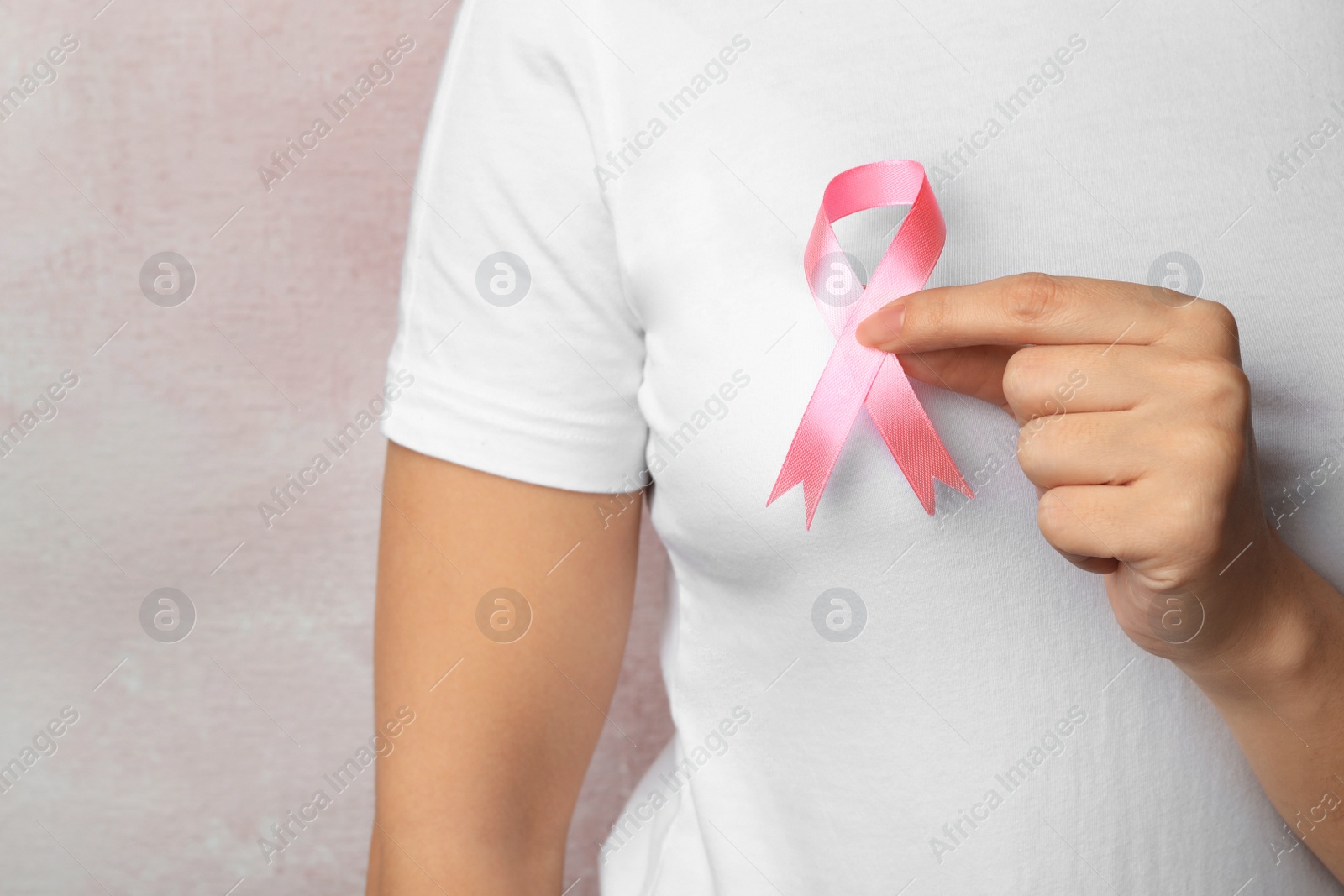 Photo of Woman holding pink ribbon on color background, closeup with space for text. Breast cancer awareness