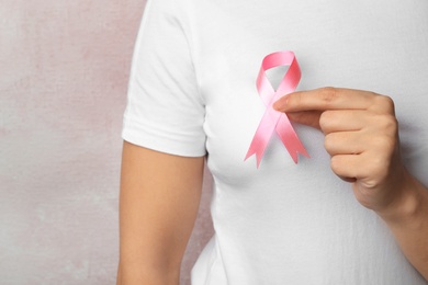 Photo of Woman holding pink ribbon on color background, closeup with space for text. Breast cancer awareness
