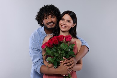 International dating. Happy couple with bouquet of roses on light grey background