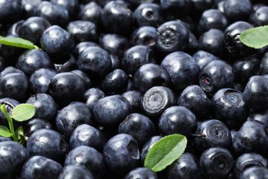 Photo of Many delicious ripe bilberries and green leaves as background, closeup