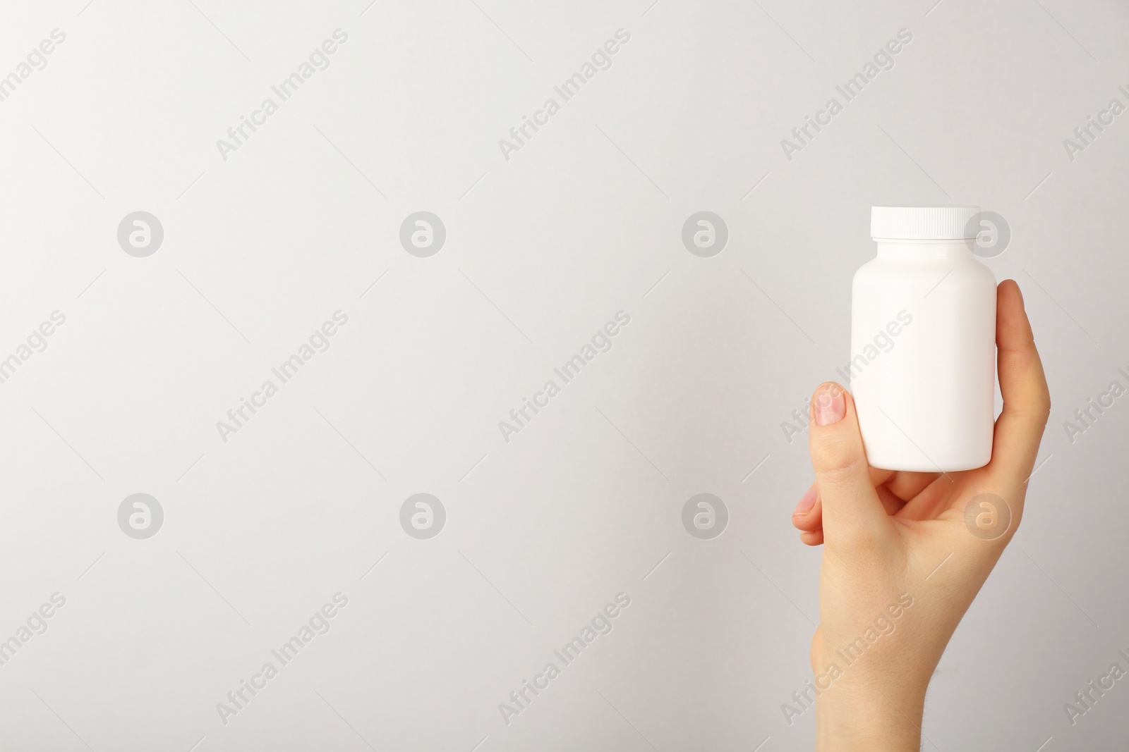 Photo of Woman holding blank white jar of vitamins on light grey background, closeup. Space for text