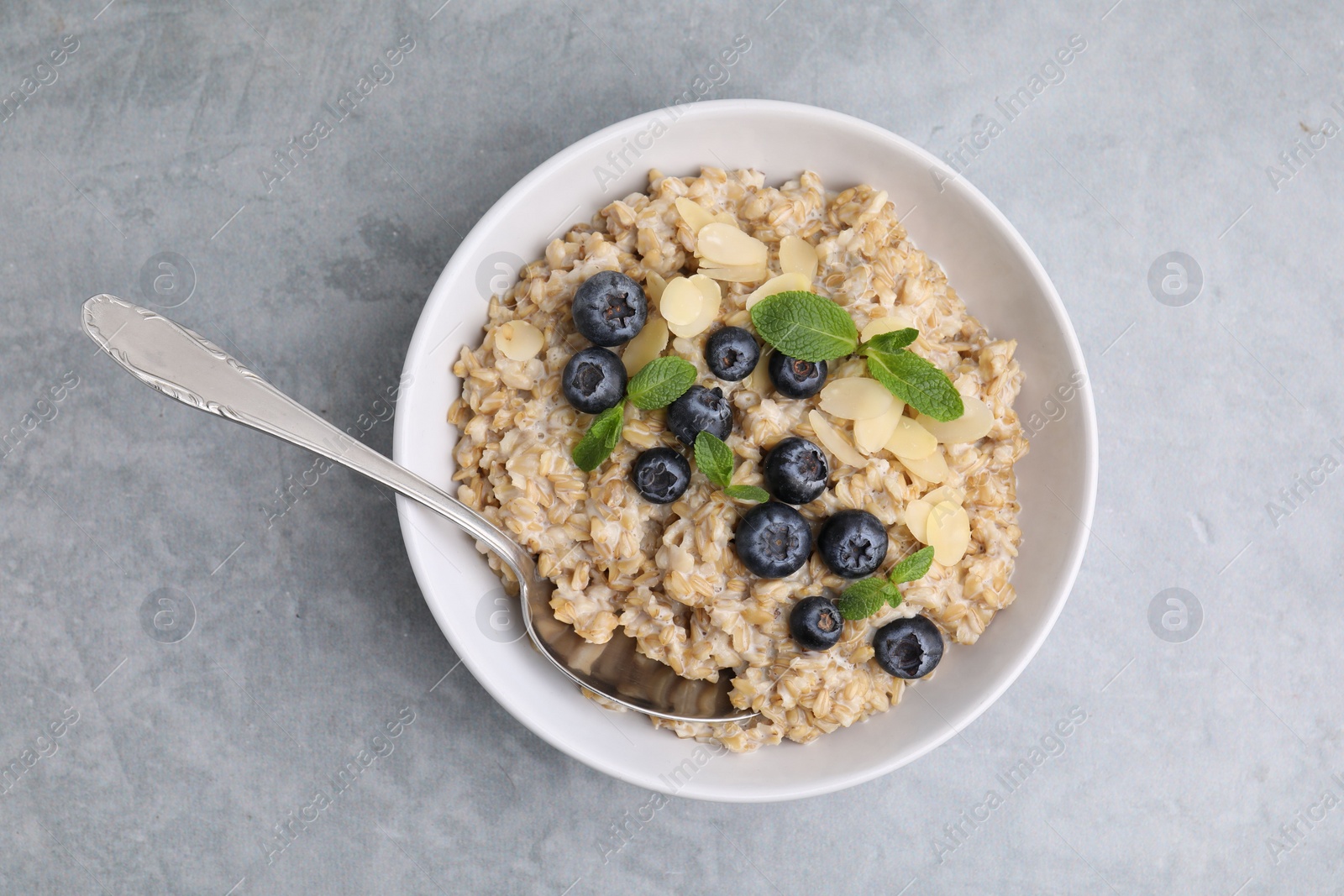 Photo of Tasty oatmeal with blueberries, mint and almond petals in bowl on grey table, top view