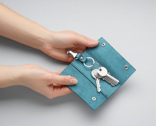 Woman holding open leather holder with keys on light grey background, top view