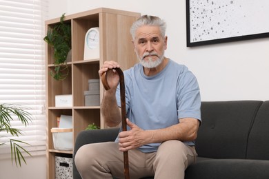 Photo of Senior man with walking cane sitting on sofa at home