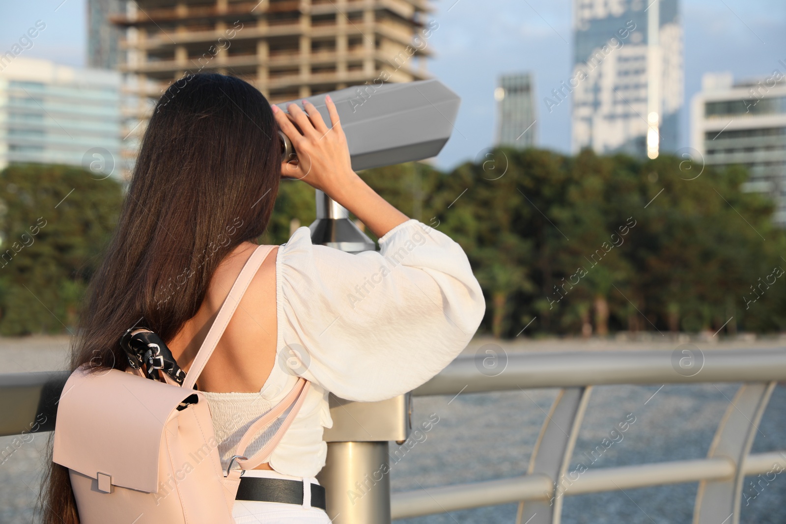 Photo of Young woman looking through tourist viewing machine at observation deck, back view. Space for text