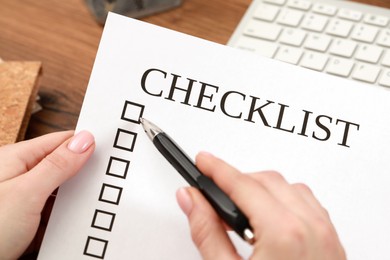 Photo of Woman filling Checklist at wooden table, closeup