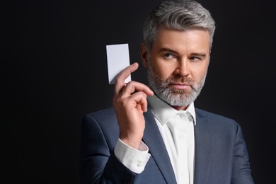 Handsome businessman holding blank business card on black background