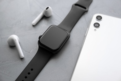 Photo of Stylish smart watch, phone and earphones on grey stone table, closeup