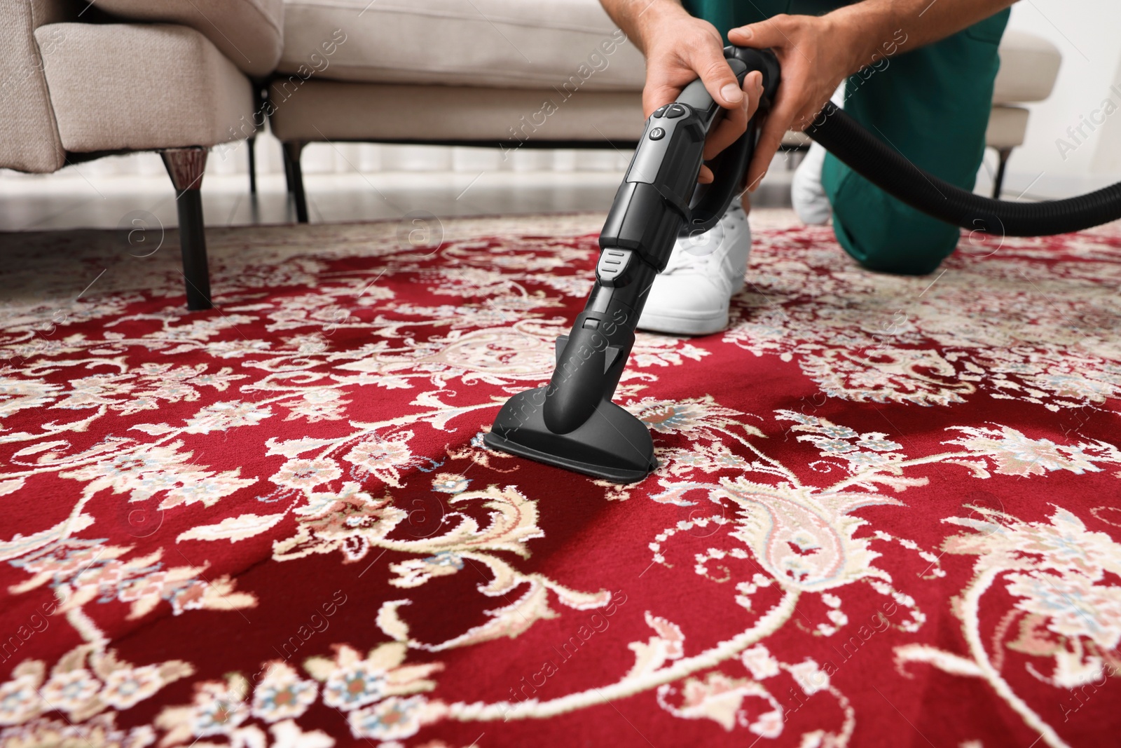 Photo of Dry cleaner's employee hoovering carpet with vacuum cleaner indoors, closeup