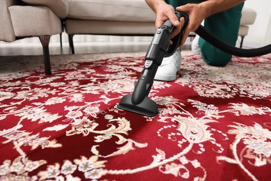 Photo of Dry cleaner's employee hoovering carpet with vacuum cleaner indoors, closeup