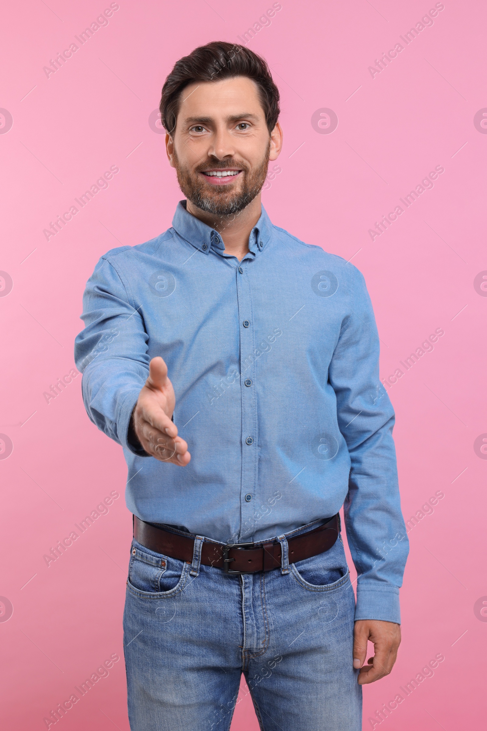 Photo of Happy man welcoming and offering handshake on pink background