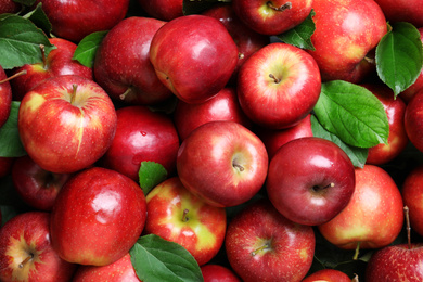 Photo of Pile of tasty red apples with leaves as background, top view