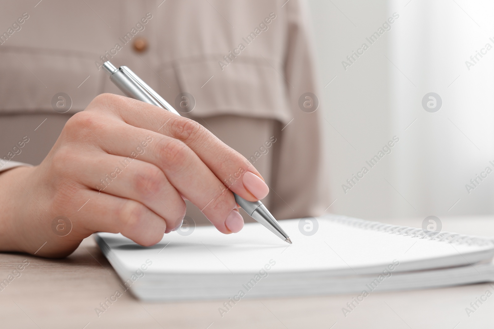 Photo of Woman writing in notebook at wooden table, closeup