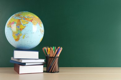 Photo of Globe, school supplies and books on wooden table near green chalkboard, space for text. Geography lesson