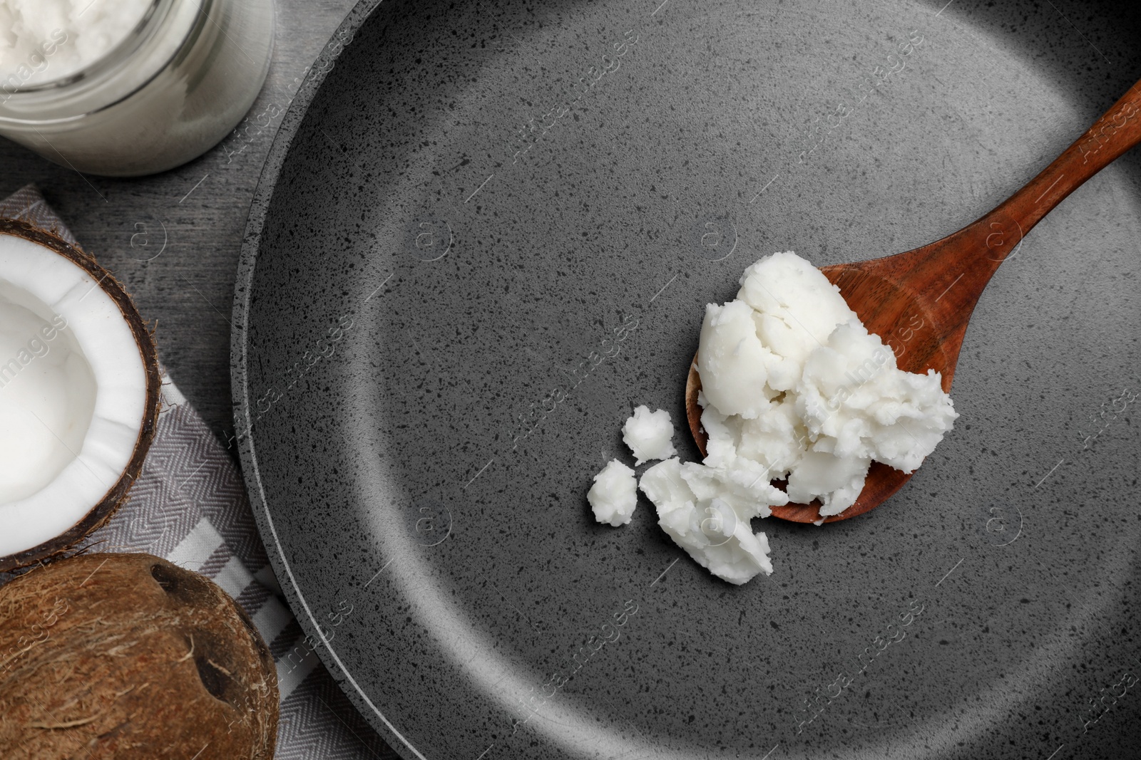 Photo of Frying pan with coconut oil and wooden spoon on grey table, flat lay