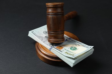 Photo of Law gavel with stack of dollars on black table, closeup