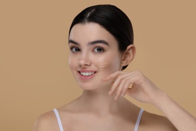 Photo of Teenage girl with swatch of foundation on face against beige background