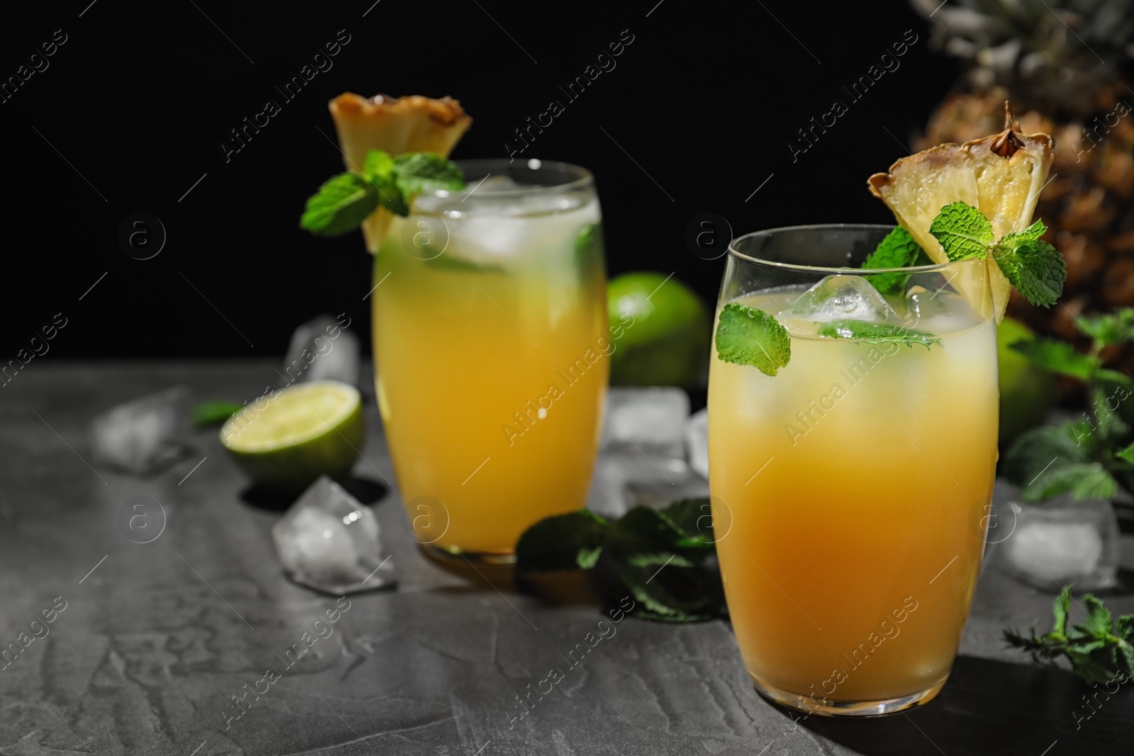 Photo of Glass of delicious cocktail decorated with ice and mint on grey table against black background