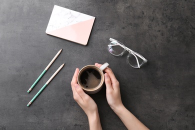 Photo of Young woman with cup of delicious hot coffee at table, top view