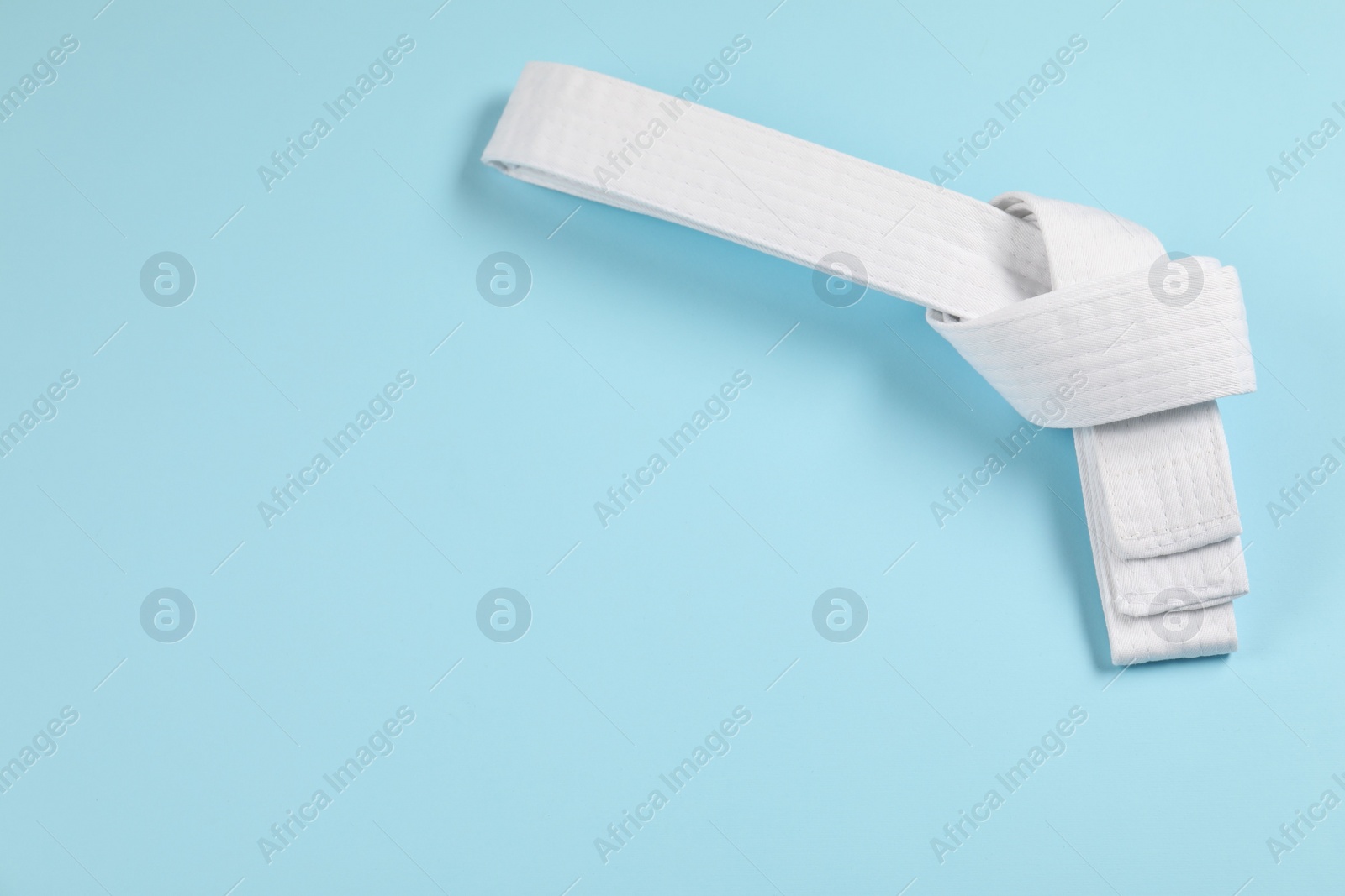 Photo of White karate belt on light blue background, top view. Space for text