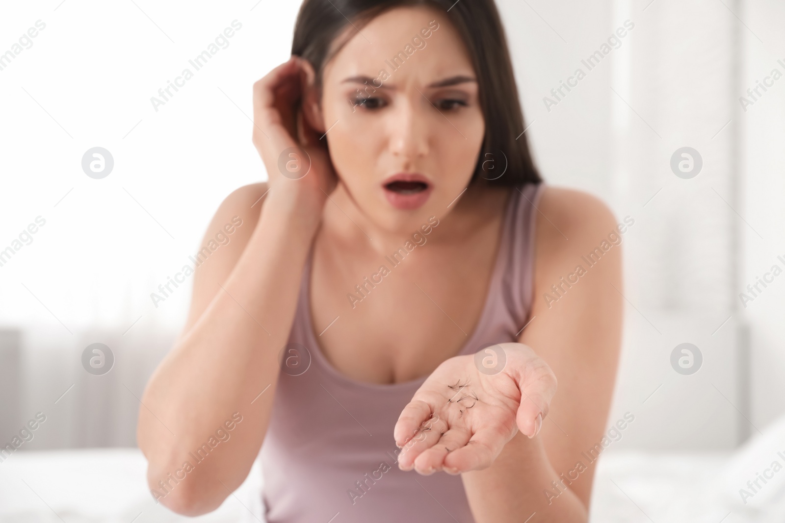 Photo of Beautiful woman holding fallen eyelashes in hand indoors