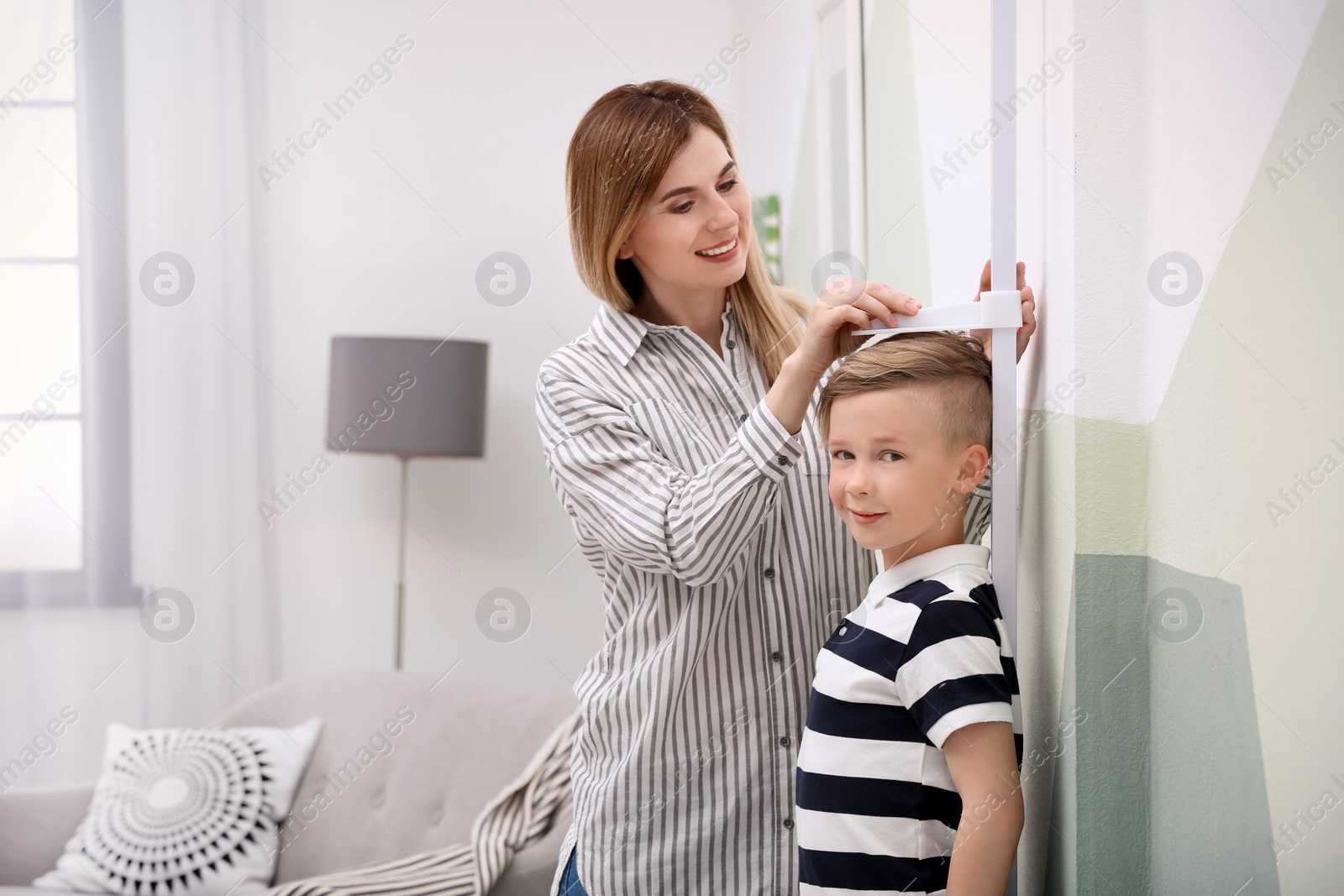 Photo of Young woman measuring her son's height at home