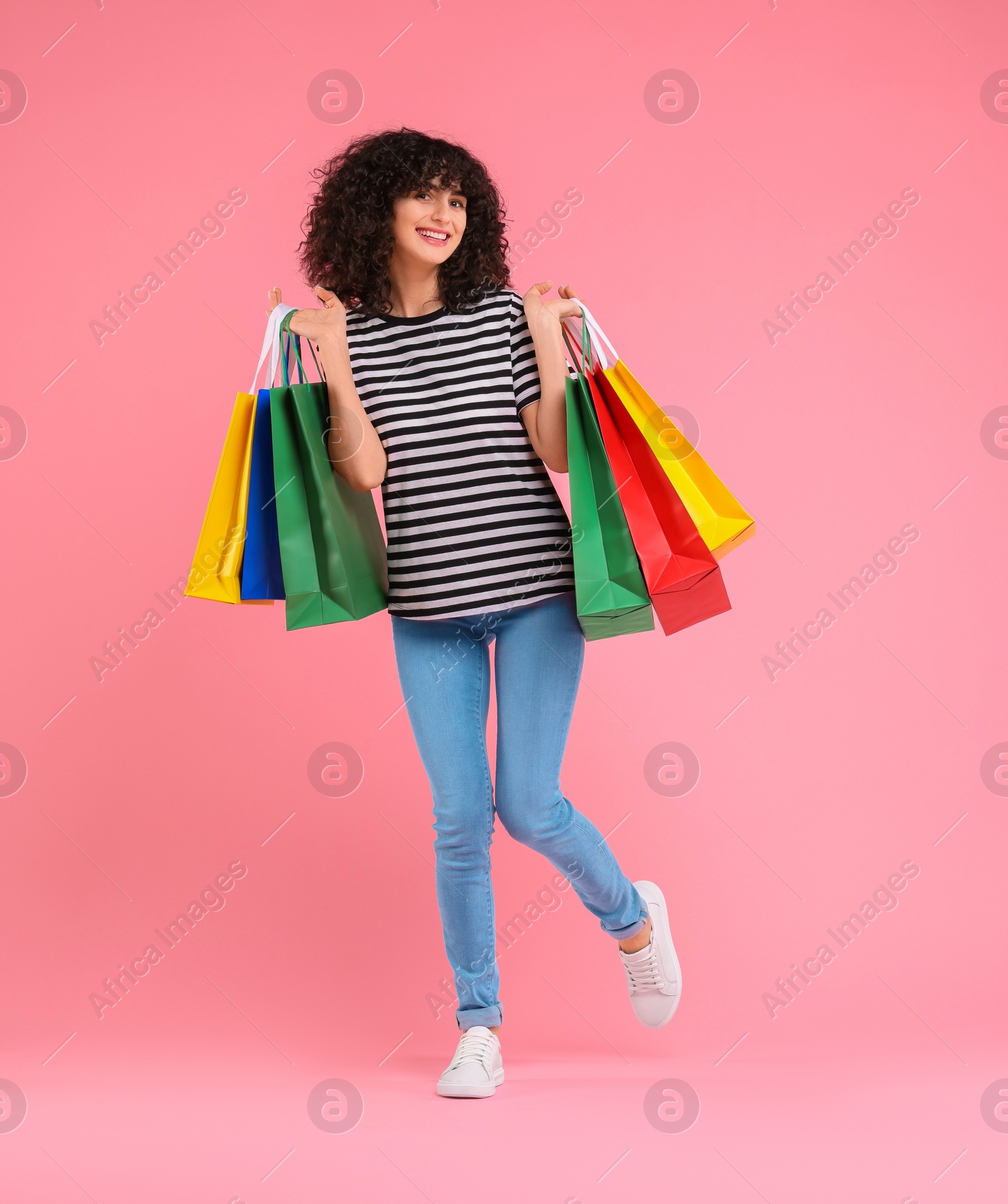 Photo of Happy young woman with shopping bags on pink background