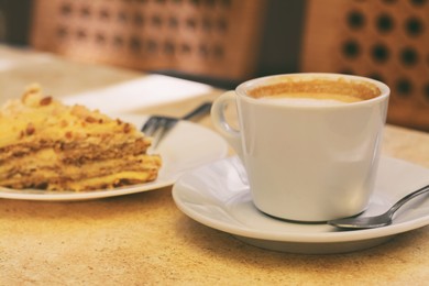 Photo of Cup of coffee and delicious cake on beige table, closeup