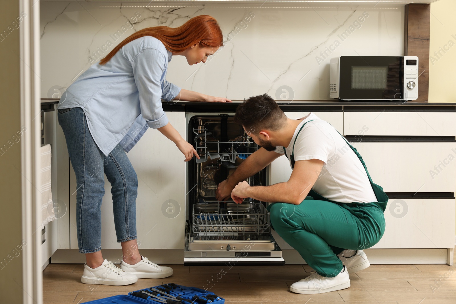 Photo of Young woman discussing with repairman near dishwasher in kitchen