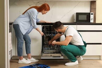 Photo of Young woman discussing with repairman near dishwasher in kitchen
