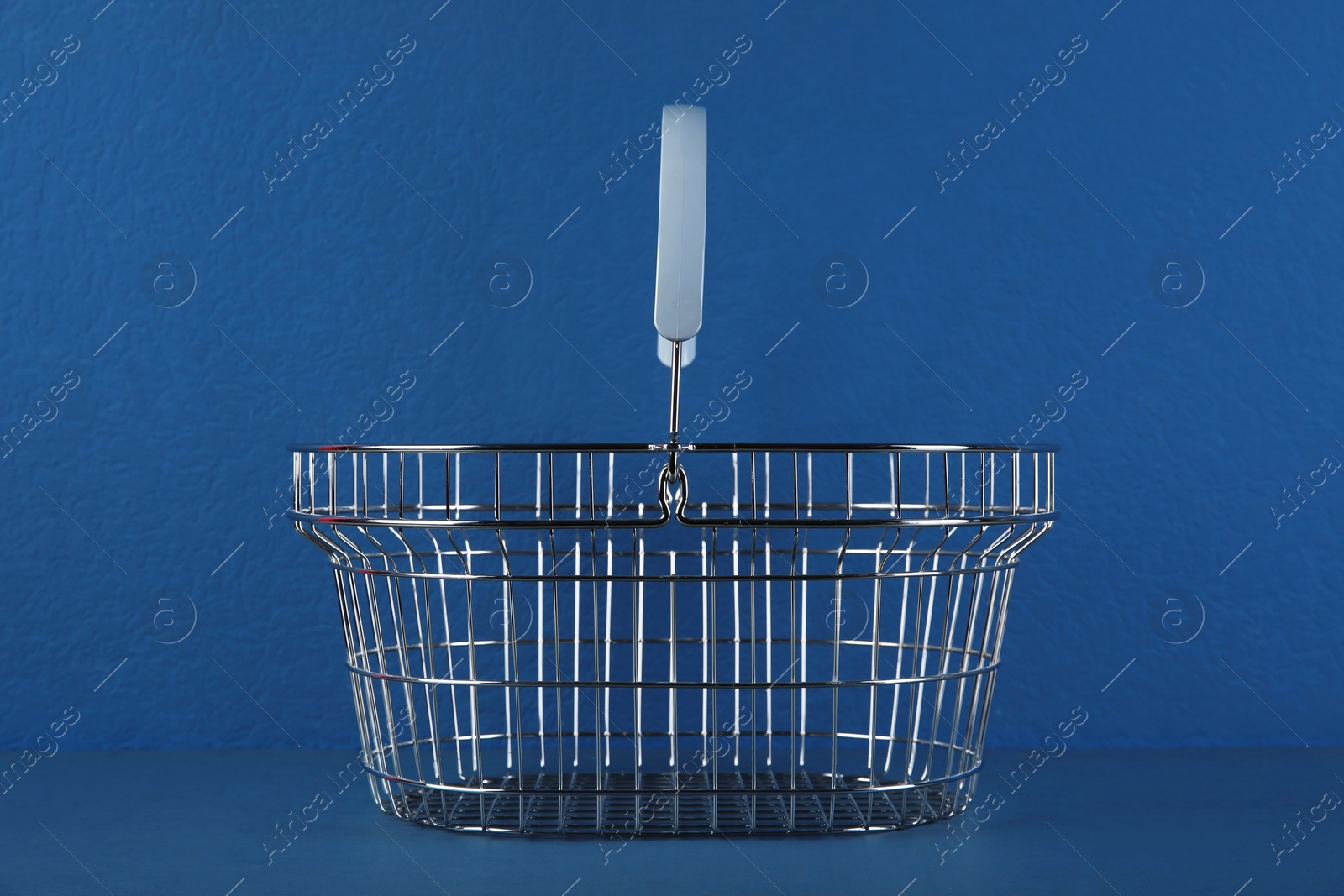 Photo of Empty metal shopping basket on blue background