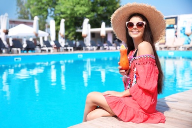 Photo of Beautiful young woman with cocktail sitting near outdoor swimming pool