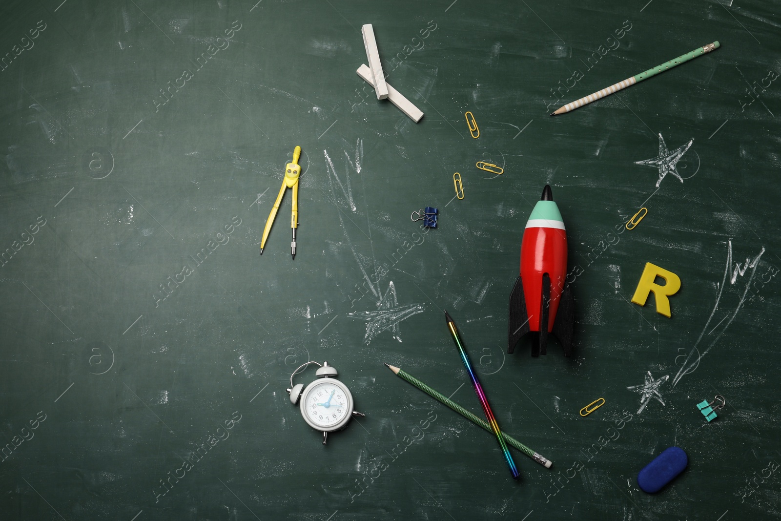 Photo of Bright toy rocket, school supplies and drawings on chalkboard, flat lay. Space for text