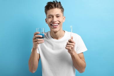 Photo of Young man with mouthwash and toothbrush on light blue background