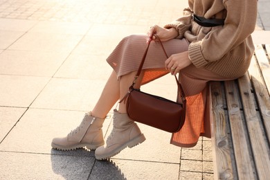 Photo of Fashionable woman with stylish bag on bench outdoors, closeup