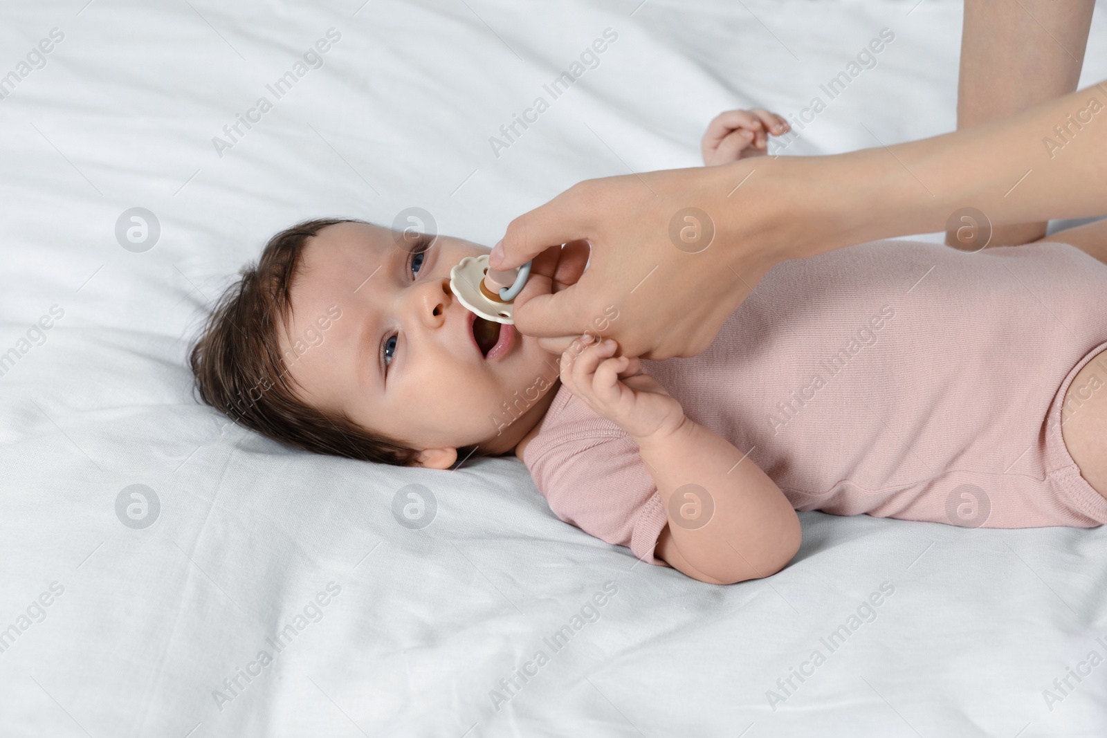 Photo of Mother giving pacifier to crying little baby on bed, closeup