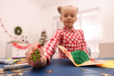 Cute little child with beautiful Christmas card at table in room, focus on decorative clothespin