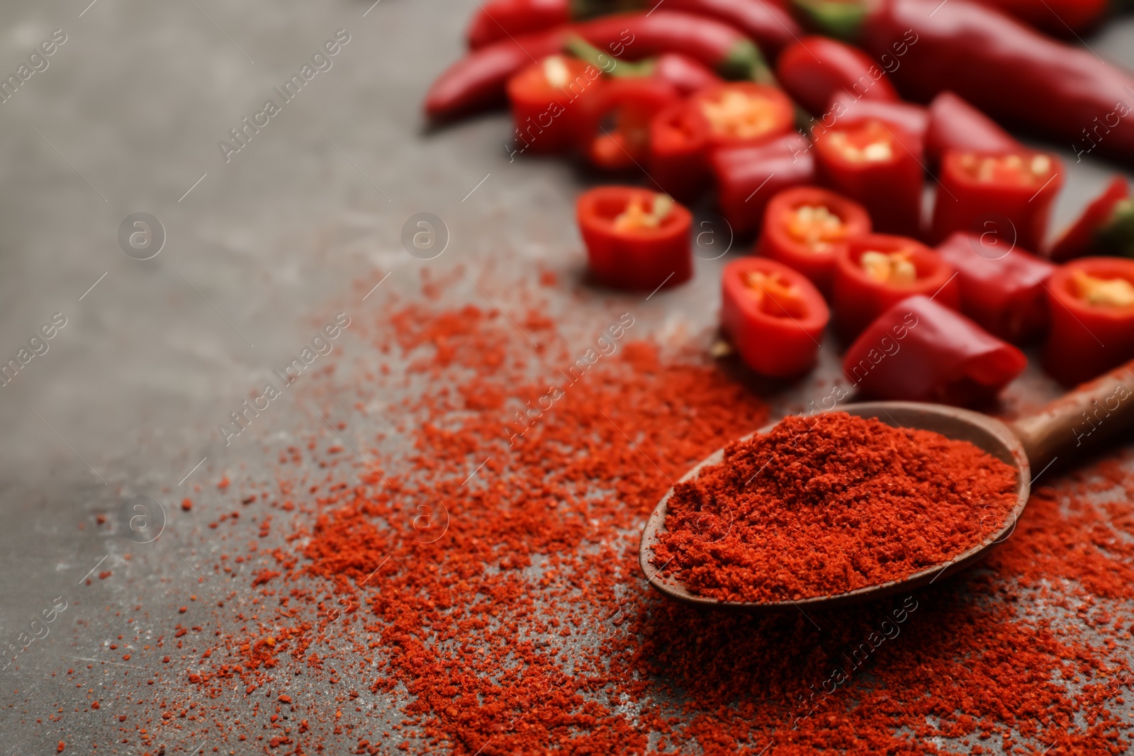 Photo of Spoon with chili pepper powder on gray table. Space for text