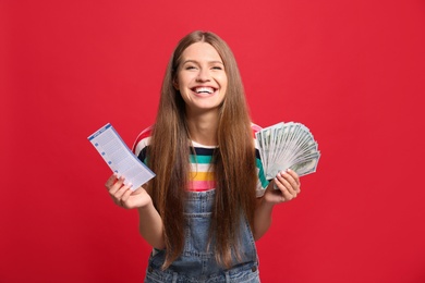 Portrait of happy young woman with lottery ticket and money on red background