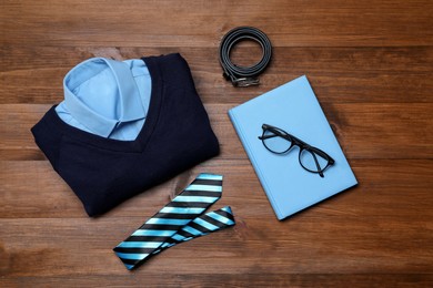 Photo of Stylish school uniform for boy, glasses and notebook on wooden background, flat lay