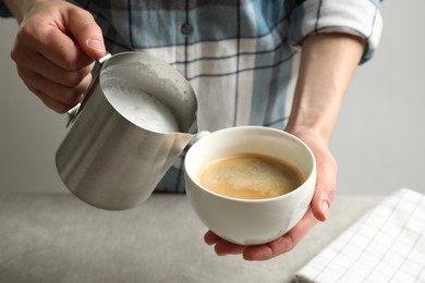 Woman pouring milk into cup of hot coffee, closeup